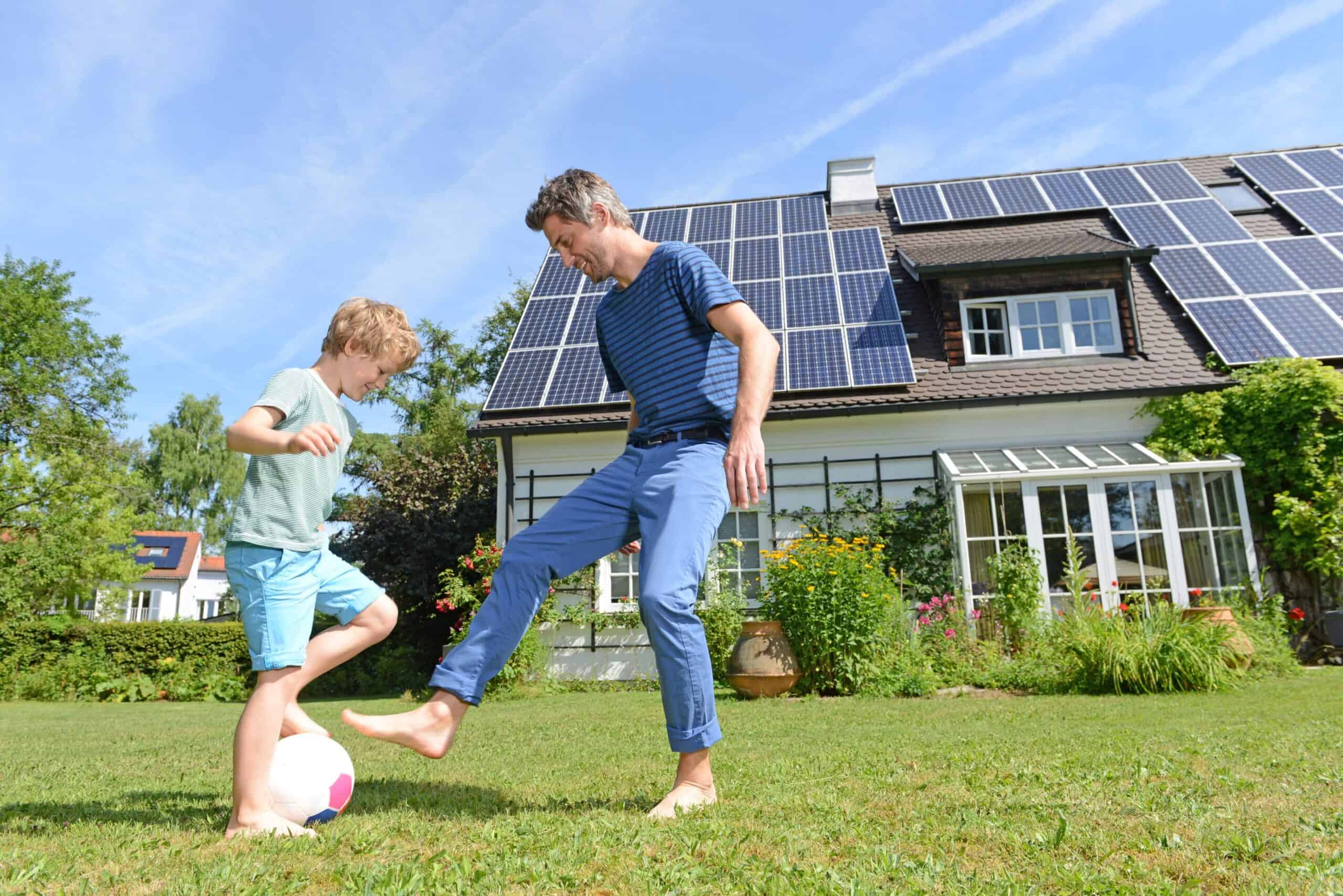Father and son playing yard soccer with solar panels in background