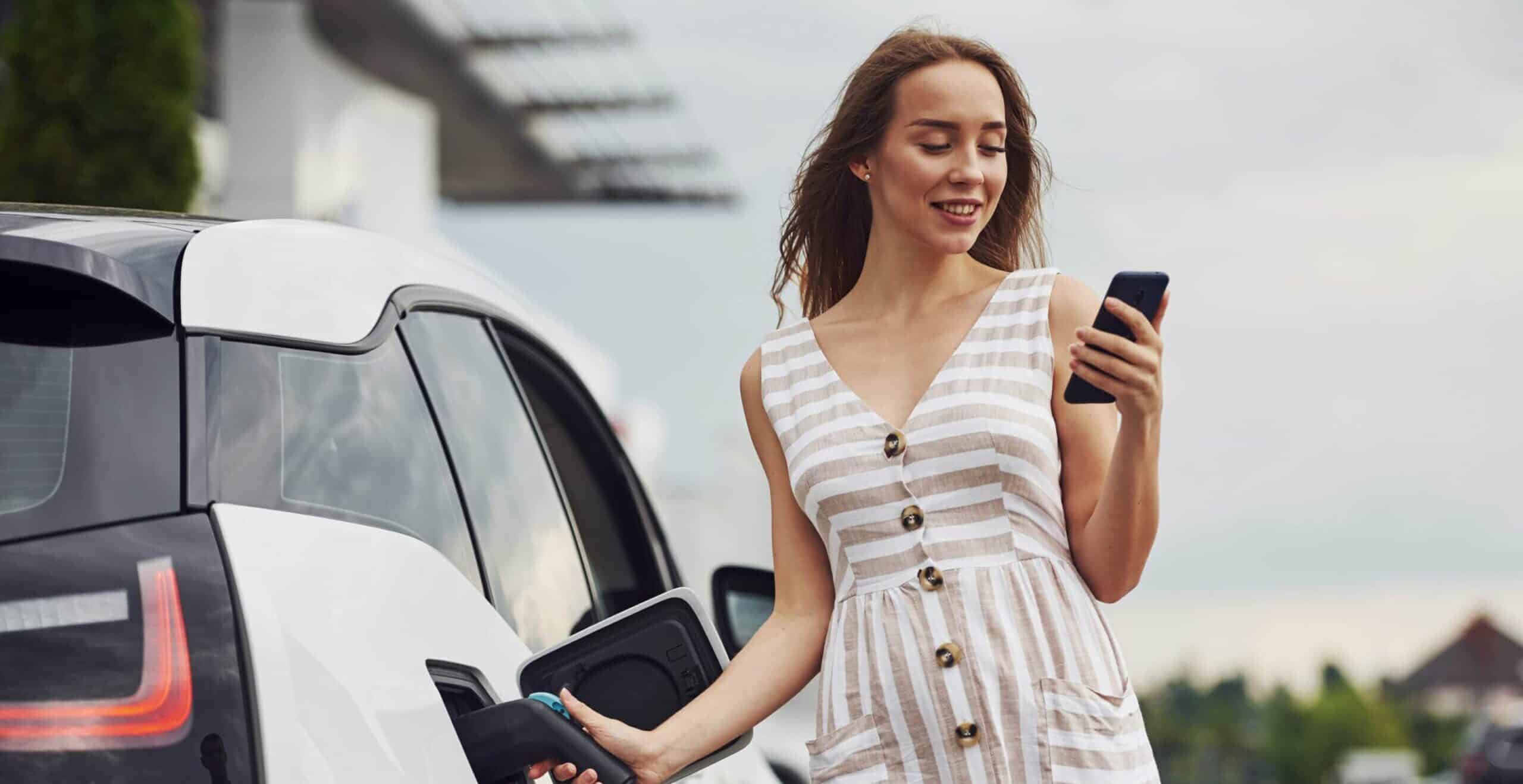 Young woman using SmartPhone & Charging EV